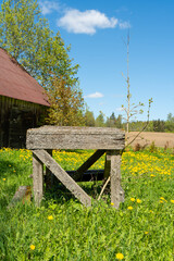 An old moss-covered wooden table in a rural landscape with dandelions, blue skies, and an old barn in the background.