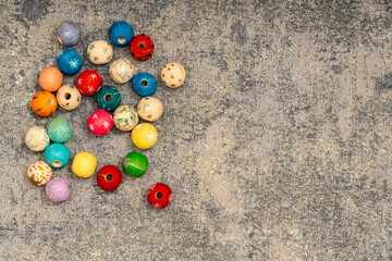 Flat lay of assorted colorful painted wooden beads scattered on a dark grey concrete or stone surface with copy space
