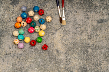 Top view of two paint brushes and scattered colorful wooden beads on a textured grey stone background. Art supplies