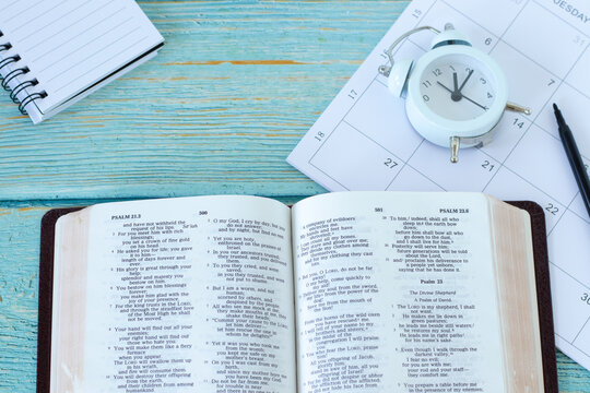 Open holy bible book with calendar, notebook and alarm clock on wooden table. Top view. Christian patience, Scripture study, biblical concept.