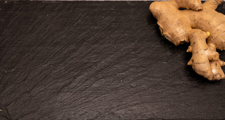 Flat lay of fresh raw ginger root on a black slate stone board with copy space. Healthy spice and herbal medicine ingredient