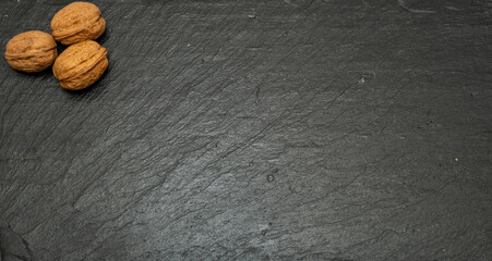 Top view of three whole walnuts in shell arranged on a dark black slate plate with ample copy space. Minimalist food shot