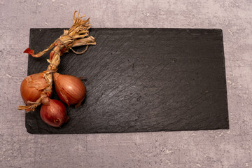 Top view of a braid of red onions or shallots on a dark black slate background with copy space. Rustic food ingredient