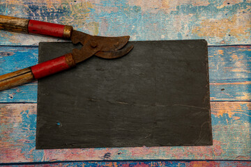 Flat lay of old rusty garden shears and a black slate board on a rustic blue peeling wood background