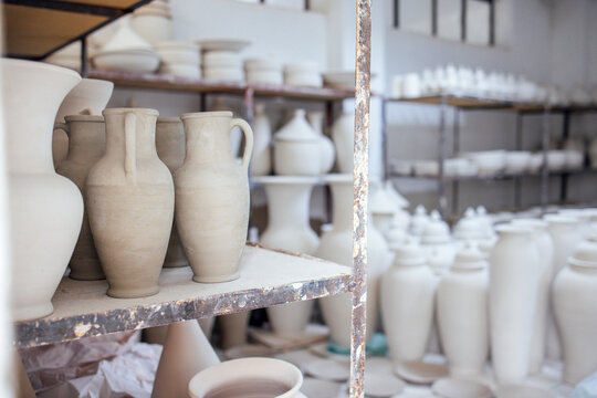 Collection of unglazed ceramic vases and pots displayed on shelves in a pottery studio, showcasing craftsmanship and artistic design in a creative workspace