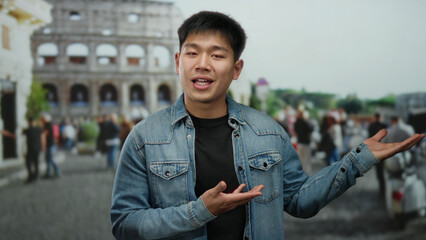 Young chinese man extends hands in front of roman coliseum in city street, blending modern fashion...