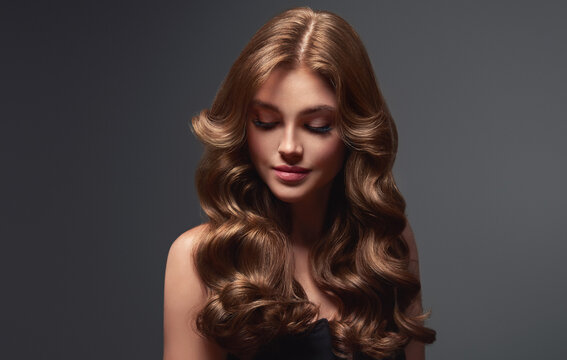 Brunette girl with long and shiny wavy hair . Beautiful model woman with curly hairstyle . Beauty and cosmetology

