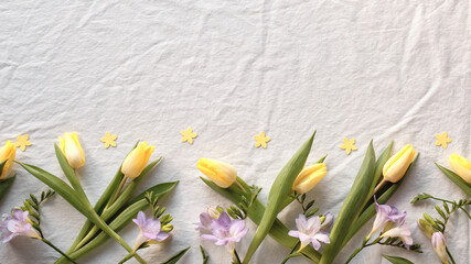 Yellow tulips and small pastel blooms lie along the lower edge on crumpled light fabric with...