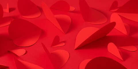 Valentine's Day background with red paper hearts. Compositions of red paper hearts of different sizes on a monochrome bright red background. Concept of love, romance, Valentine's Day holiday.