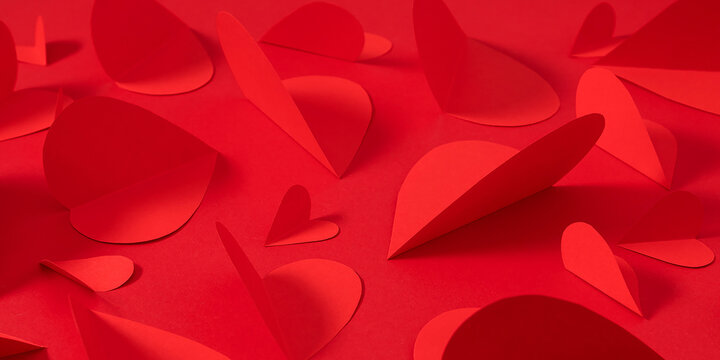 Valentine's Day background with red paper hearts. Compositions of red paper hearts of different sizes on a monochrome bright red background. Concept of love, romance, Valentine's Day holiday.
