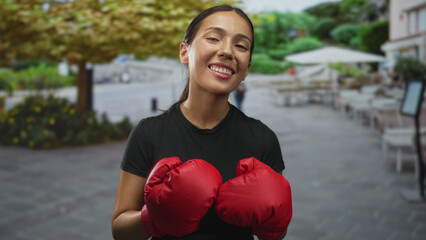 Young woman boxer with red boxing gloves smiling on a restaurant terrace; confidence empowerment resilience.