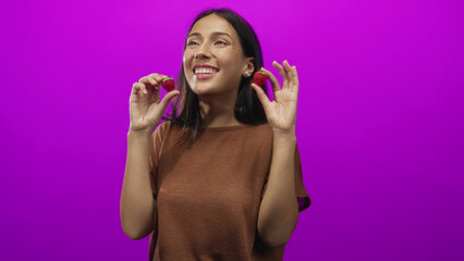 Woman holding two strawberries with hands near face in studio with magenta background smiling and eyes closed; joy freshness.