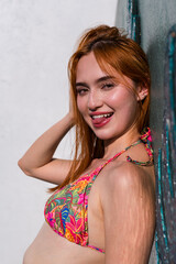 Fototapeta premium Smiling woman leaning on wall in colorful bikini top