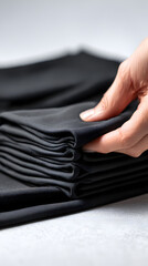 Hand Folding Stacked Clothes: A hand meticulously folds and stacks a pile of dark clothes, creating a sense of order and cleanliness.