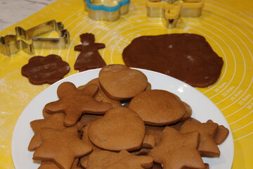 Cookies are cut into shapes with various cutters on a yellow mat in a kitchen