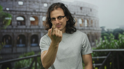 Fototapeta premium Man showing middle finger to camera on a building terrace near the colosseum, tshirt and glasses; defiance provocation insult.