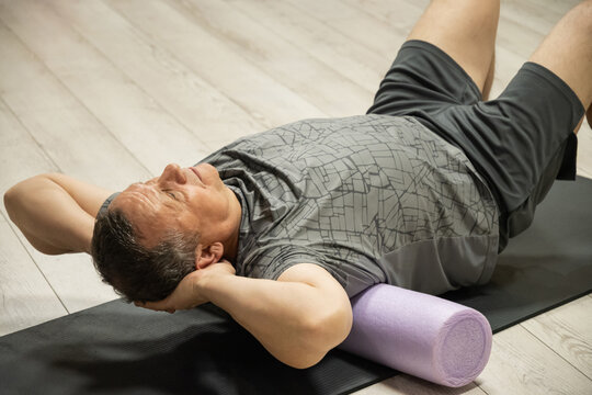 Adult man practicing relaxation exercise on foam roller, stretching and easing back tension during a yoga session for healthy mobility.
