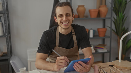 Man sketching on tablet with stylus in studio, hands on screen and pottery tools on table; focused creativity.