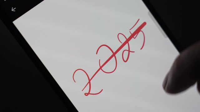 Finger crossing out the handwritten red &ldquo;2025&rdquo; on a smartphone screen, symbolizing the end of the year, closing a chapter and visually marking the transition toward a new beginning.