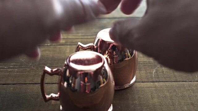 Two copper cups are stacked on a wooden table. Hands reach to place them together playing shell game or thimberling about pill