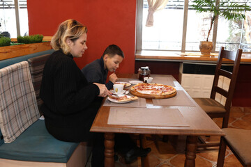 A woman and a boy are eating delicious pizza and drinking tea in a pizzeria.