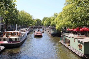 Obraz premium Sunny Day on an Amsterdam Canal with Houseboats and Tour Boats