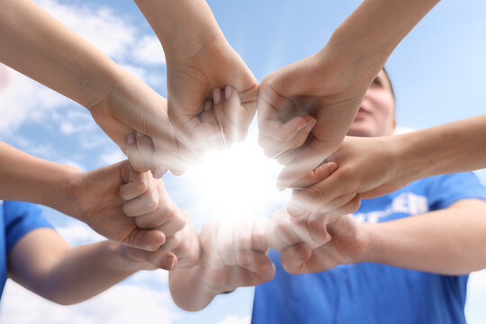 Group of volunteers bumping fists outdoors on sunny day, closeup