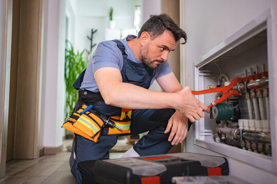 Plumber fixing central heating pipes with red pipe wrench