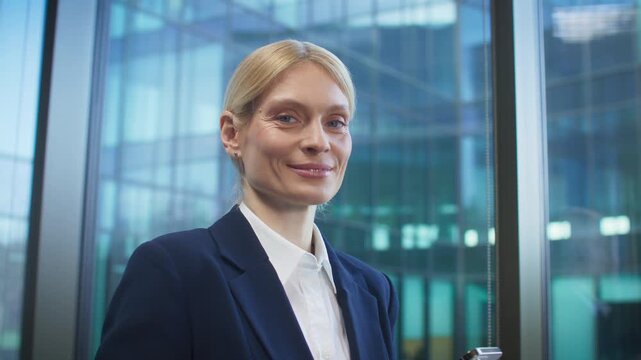 Confident blonde Caucasian businesswoman holding smartphone. Getting briefly distracted and making eye contact with camera. Pausing in the middle of a task. Looking directly and smiling.