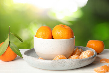 Fresh juicy tangerines on white table against blurred green background
