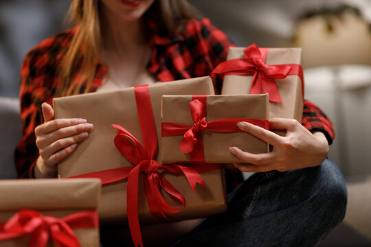 A woman in a red plaid shirt holds several wrapped gifts with red ribbons, perfect for a special occasion