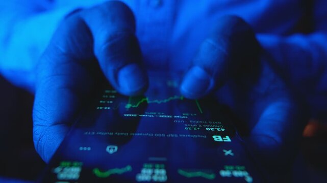 Businessman hands checking financial stock market charts on a mobile phone in a dark blue room