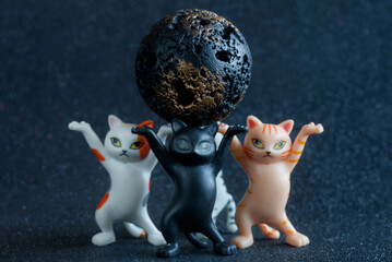 Funny toy kittens holding a textured black asteroid on a starry background. Creative astronomy concept about meteorite discovery or space danger. Photo