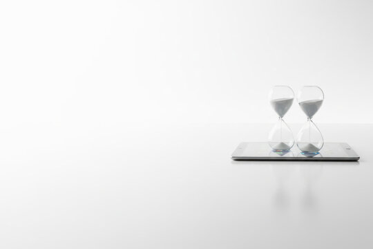 Two hourglasses standing on a tablet, on a white background. Space for text.