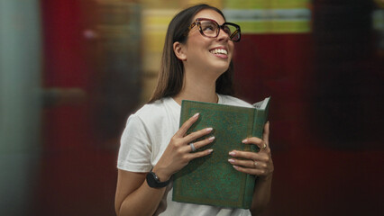 Woman reading book, hands holding pages, smiling, wearing glasses and white t shirt in train...