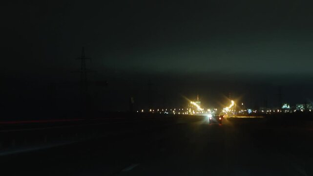 Night Highway With Distant Illuminated Interchange And Overhead Signs, Headlights Streaking Across Wet