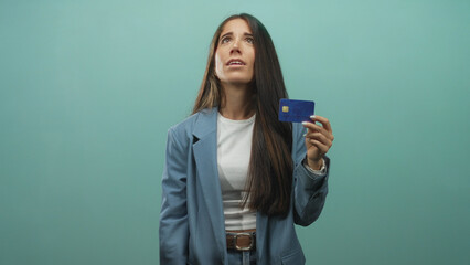 Woman holding blue creditcard up with concerned expression, presenting the card in studio wearing blue blazer and white top; financial anxiety.
