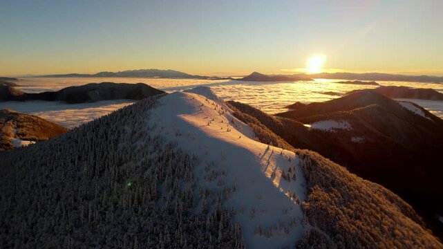 Aerial hyperlapse forward flight over snowy mountain ridge above cloud inversion at sunrise