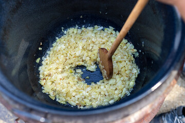 Stewed onion in a large pot with juice and sauce. Hot cooked vegetable. Cooking goulash in nature. Background