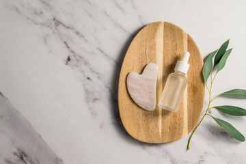 Rose quartz gua sha tool and oil bottle on wooden tray, face massage tool, beauty abstract photo. Copy space