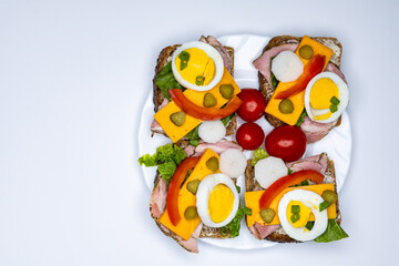 Healthy sandwiches made from whole wheat bread with egg, pickles, tomato, and chives arranged on a white plate. The plate with the sandwiches is placed against a white background.