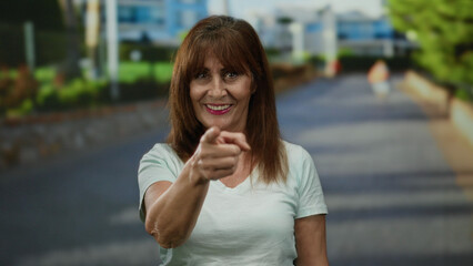 Fototapeta premium Woman smiling and pointing energetically in an urban outdoor city street, capturing a lively and engaging moment with a vibrant expression under sunny skies.