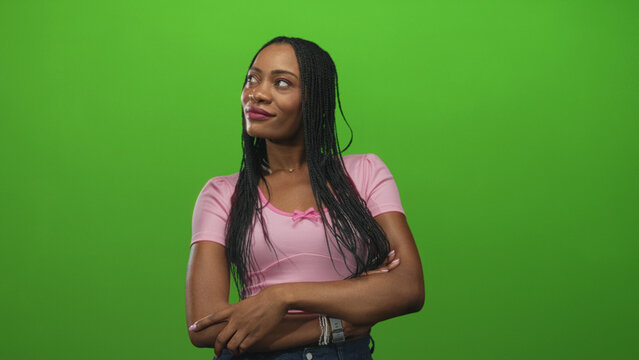 Woman with folded arms showing hands and forearms in a pink shirt against a green screen studio backdrop, slight smile and side glance; thoughtful reflection. - Powered by Adobe