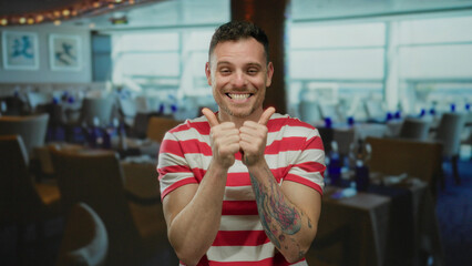 Young man with tattoos laughing enthusiastically in a vibrant restaurant setting with modern decor,...