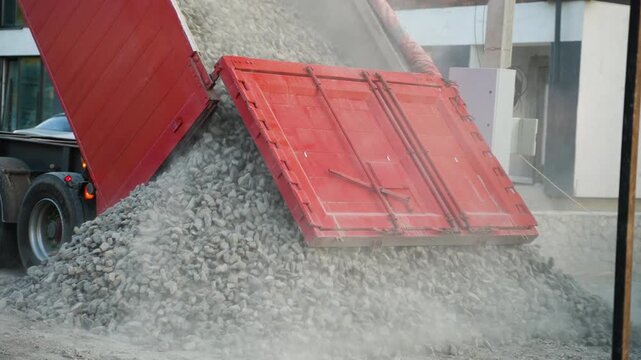 Heavy dump truck unloading crushed stone gravel at a construction site