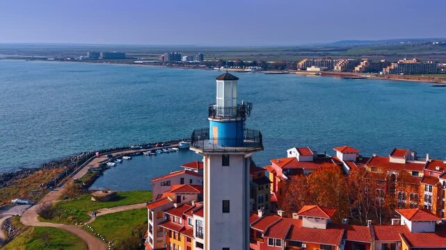 Aheloy lighthouse towers over the red-roofed houses in Marina Cape complex. Aerial perspective on the dam with the berth for boats and vast Black Sea waterscape in Bulgaria.