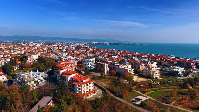 Flight over the bright urban landscape of Aheloy, Bulgaria on sunny day. Mountain range and blue seascape at backdrop.