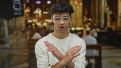 Man with crossed arms wearing white sweater stands inside church building under stained glass windows showing denial  rejection. © Krakenimages.com