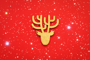 A deer head on a red background with bright lights. A decorative wooden figurine. A symbol of Christmas. Concept: Christmas, New Year, gifts, holidays. Minimalism. Flat lay.