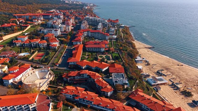 Beautiful hotels with red roofs on the green slopes of the rocks. Flight along the sunny sandy beach of the Black Sea in Nessebar, Bulgaria.
